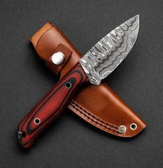 Knife with a red handle and damascus blade in a brown leather sheath on a dark background